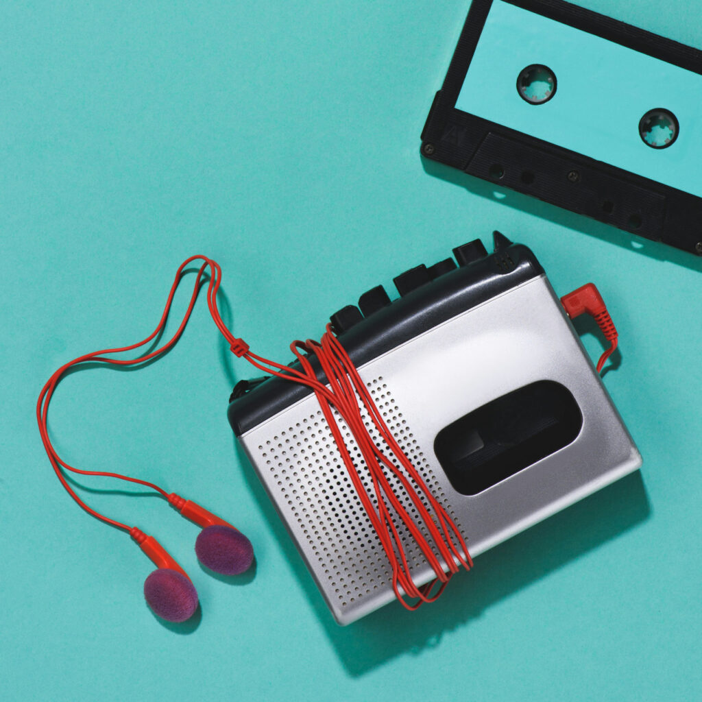 Ein silberner Walkman mit roten kabelgebundenen Ohrenstöpselkopfhörern und einer Kassette, die daneben liegt 