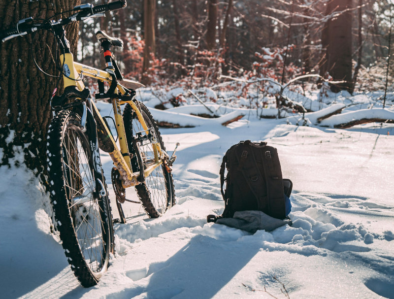 Ein Mountainbike an einen Baum gelehnt. Es liegt Schnee. Etwas daneben liegt ein Rucksack.